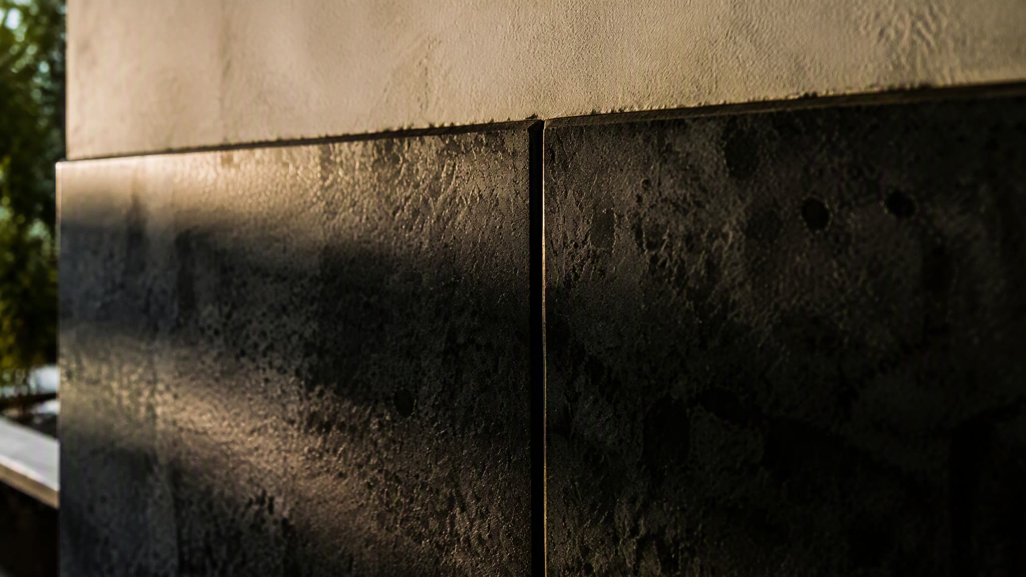 Close-up of a volcanic basalt wall joint, dark stone fitted against a hardwood screen track.
